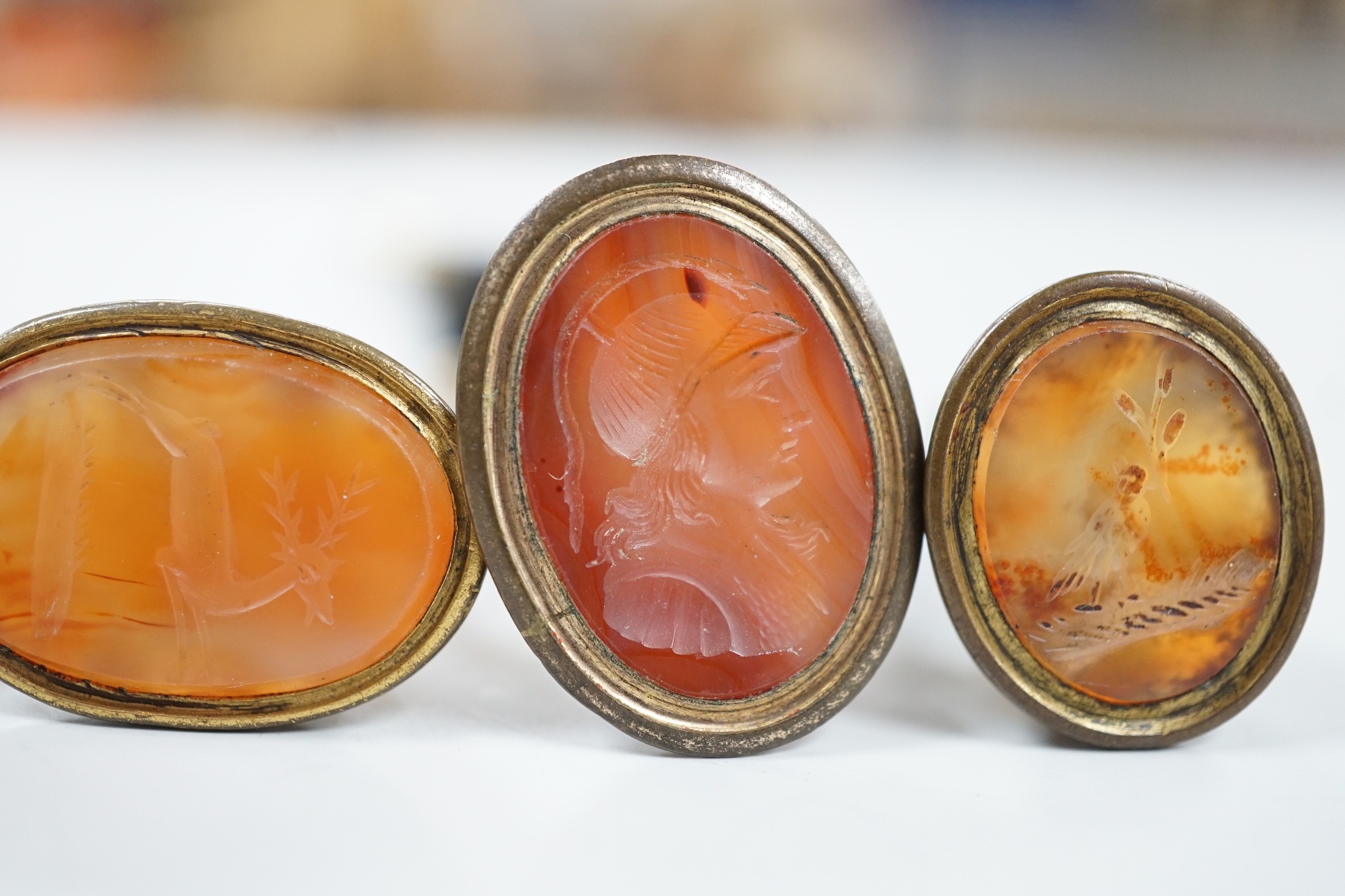 Four assorted 19th century gold plated and agate or hardstone set oval fob seals, largest 37mm, two matrices carved with busts and two with animals.